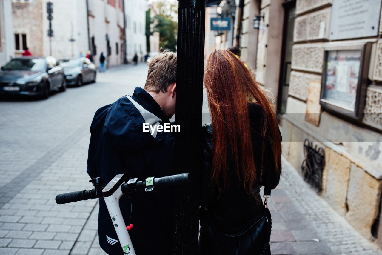 REAR VIEW OF WOMEN WALKING ON FOOTPATH IN CITY