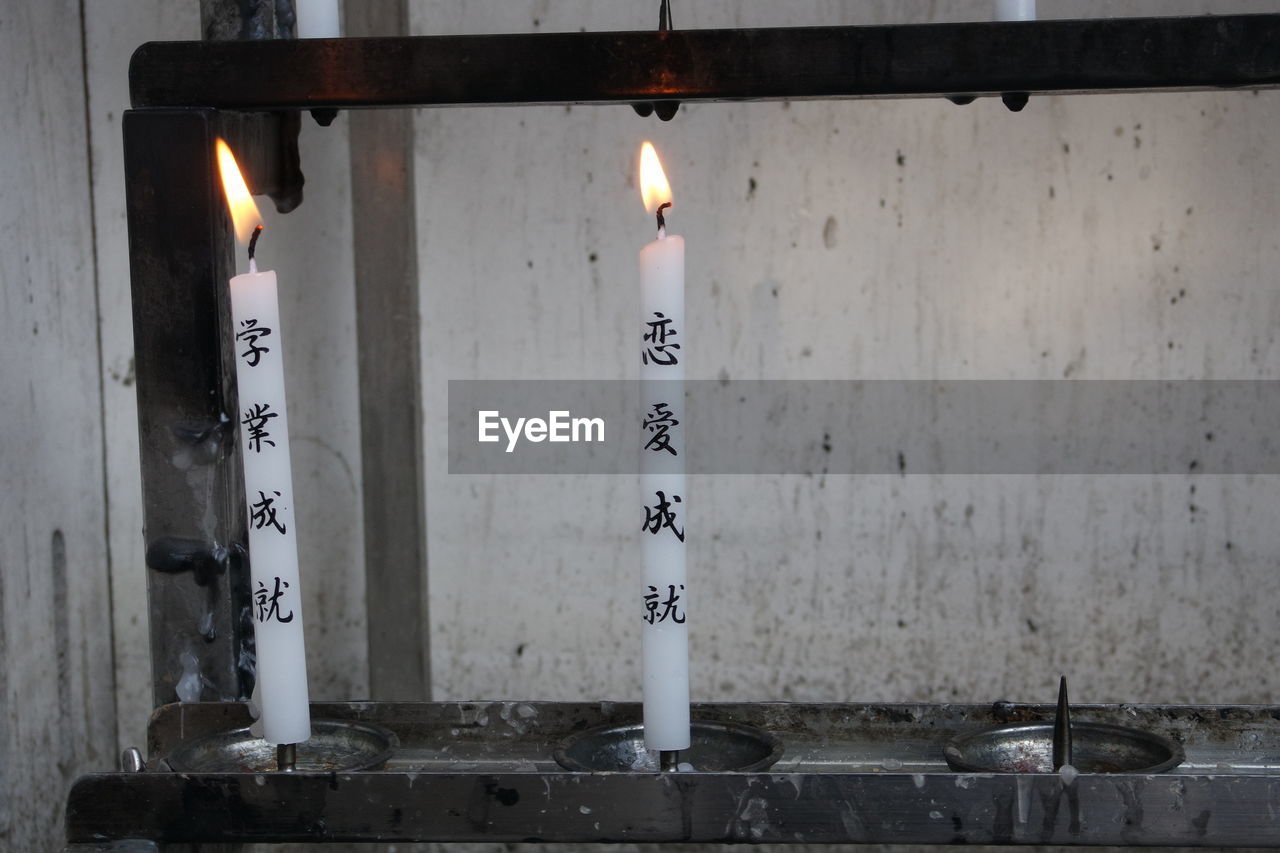 Close-up of lit candles with text burning in japanese temple