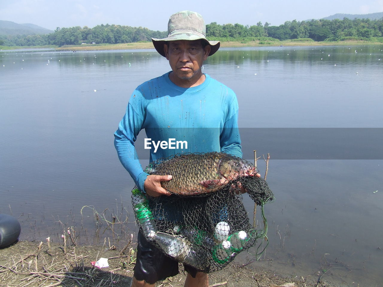 Portrait of fisherman holding fish at lake