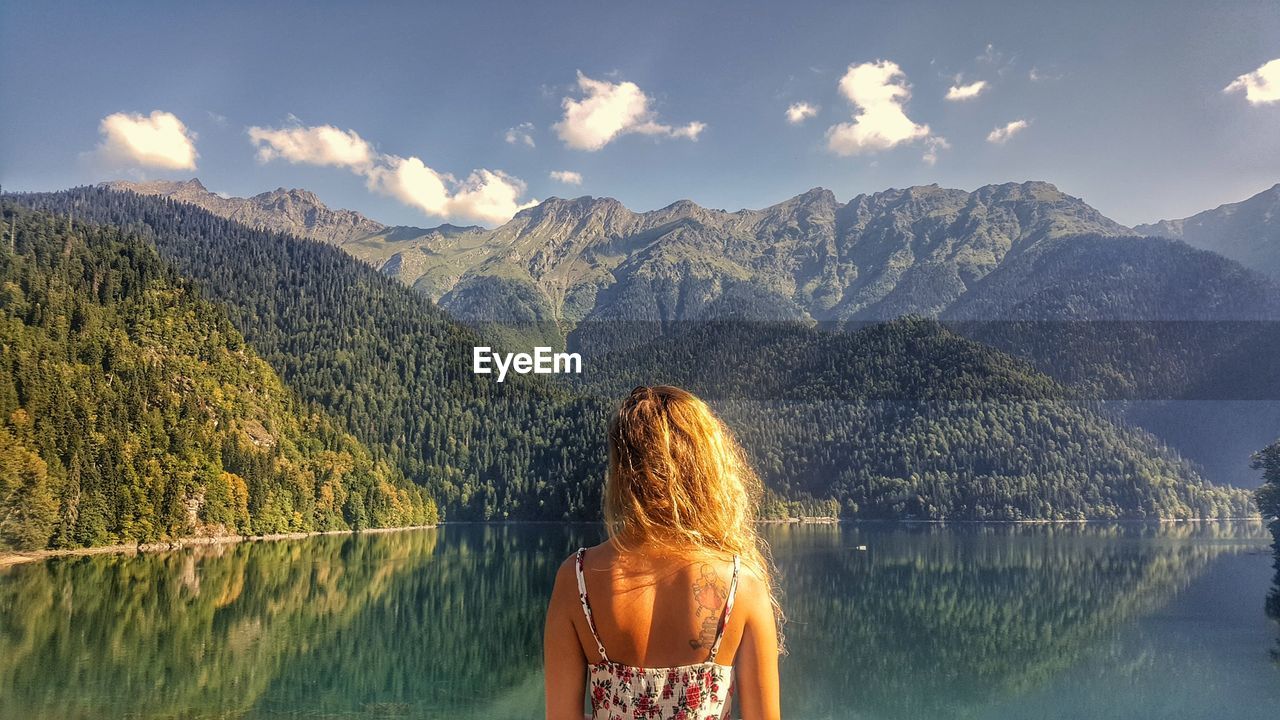 Rear view of woman standing by lake against sky