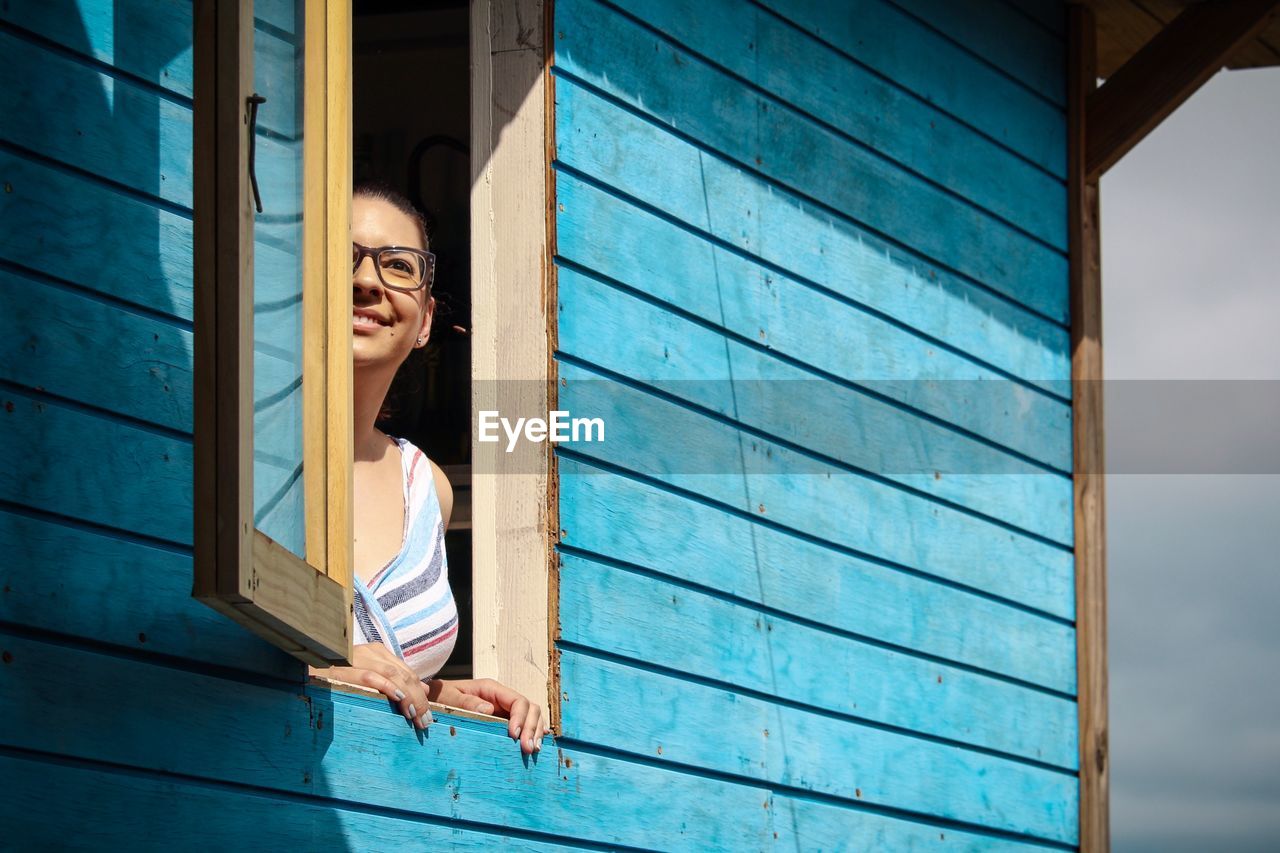 Smiling young woman looking through house window