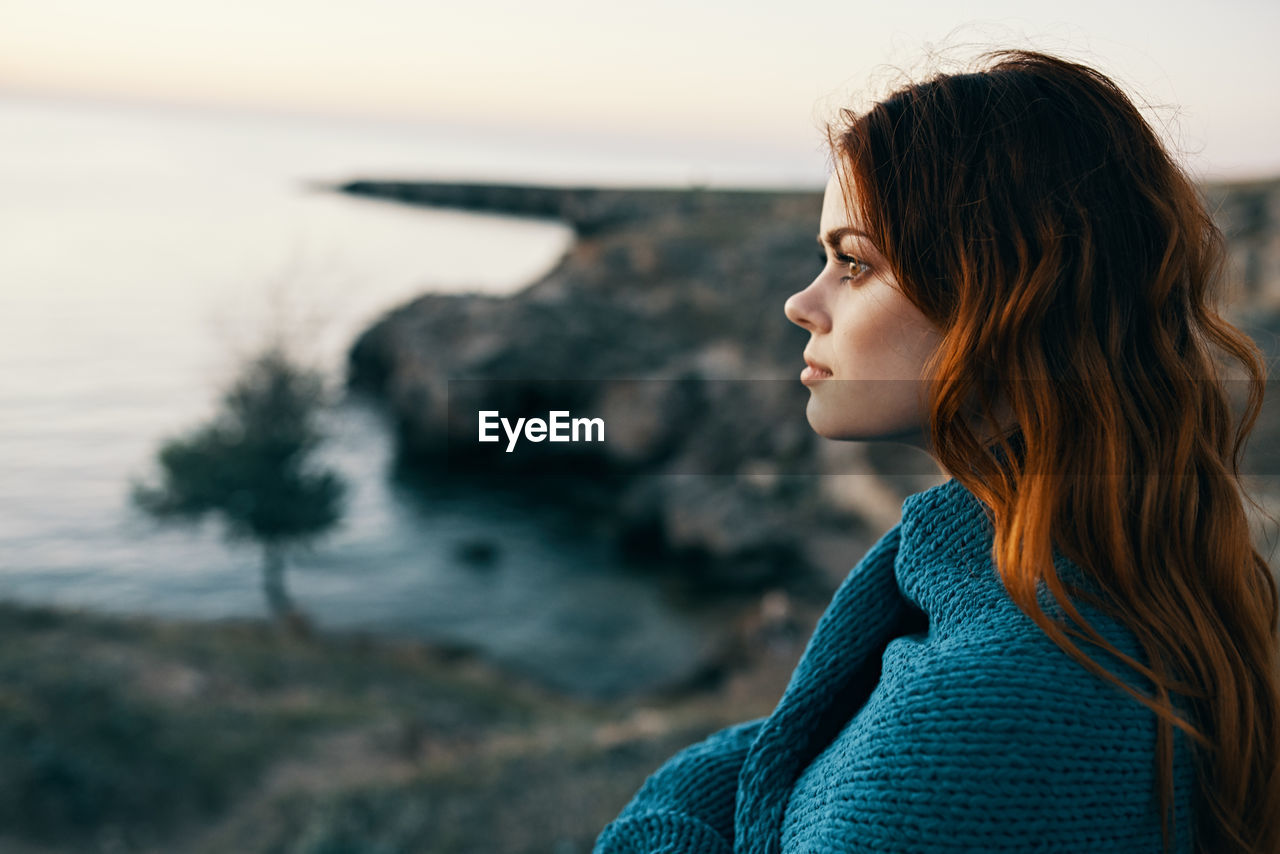 SIDE VIEW OF BEAUTIFUL YOUNG WOMAN LOOKING AWAY AT SEA