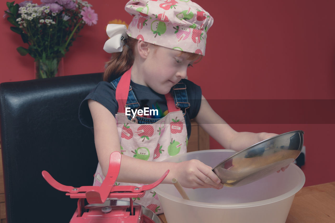 Girl wearing apron mixing flour in container on table at home