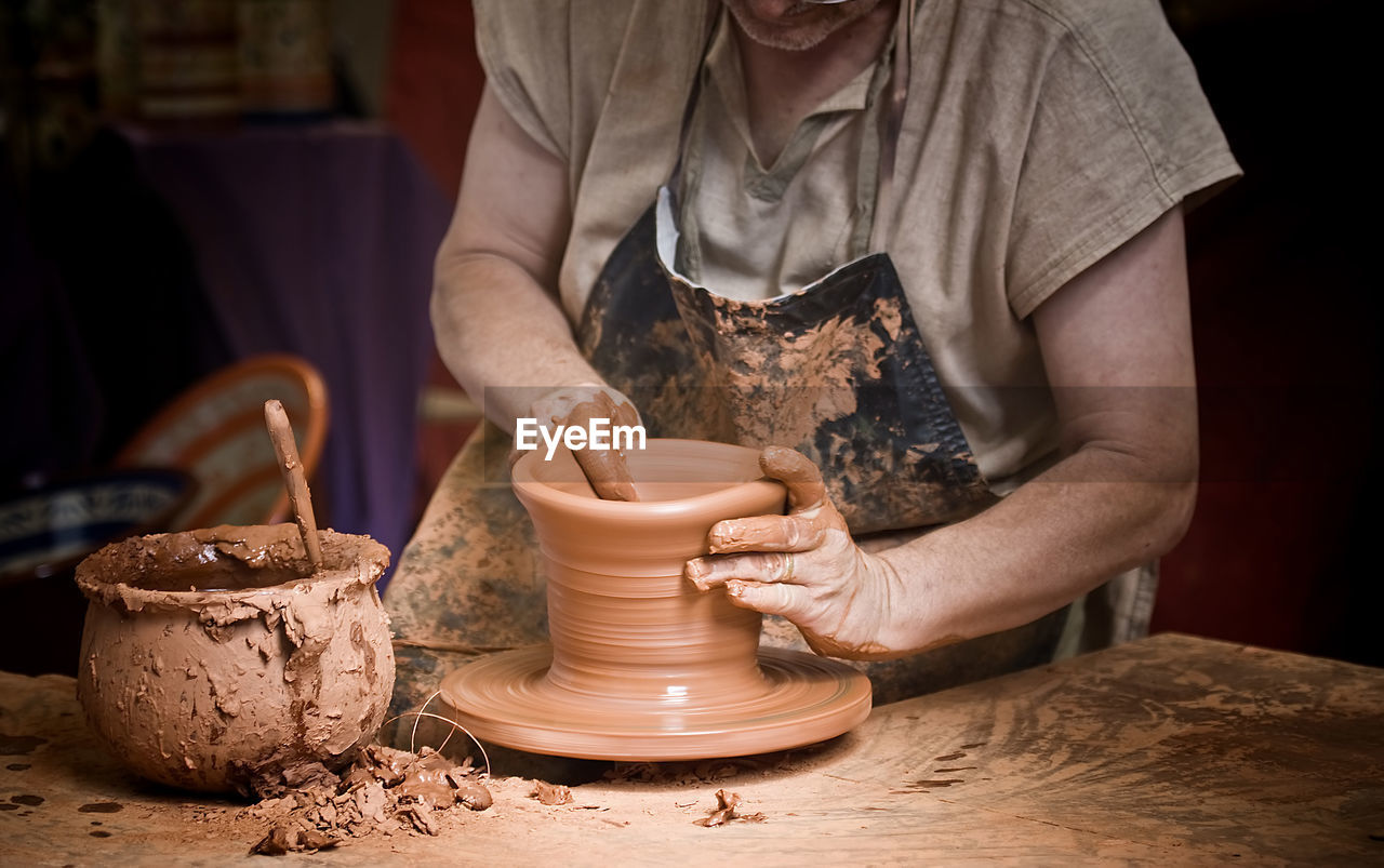 Midsection of man making pot on wheel