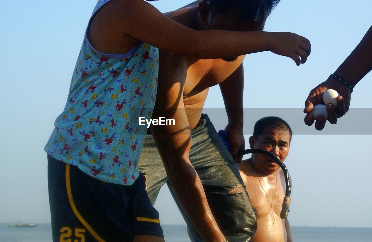adult, togetherness, water, men, women, group of people, sea, sky, nature, beach, bonding, vacation, leisure activity, fun, emotion, young adult, small group of people, lifestyles, child, day, female, friendship, standing, trip, childhood, three quarter length, summer, holiday, family, clear sky, positive emotion, parent, land, happiness, clothing, person, outdoors, casual clothing, enjoyment, love, blue, sunlight, holding