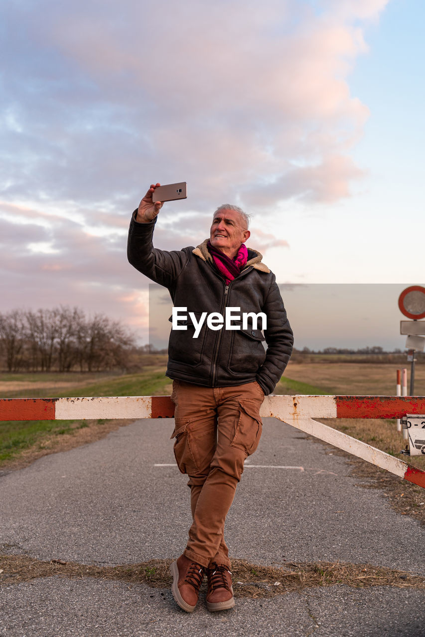 Middle aged man wearing winter clothes taking a selfie in a country road - people in recreation