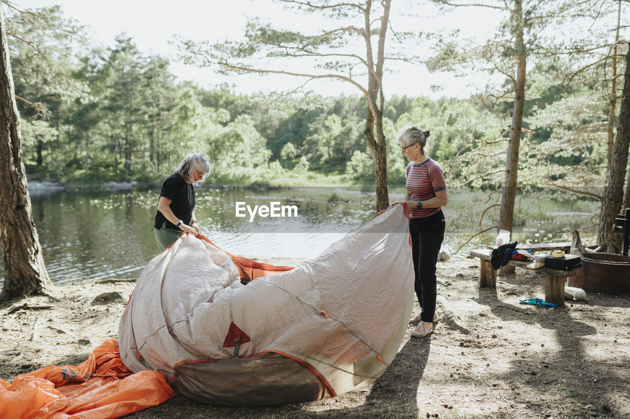 Two senior women setting up tent at campsite at lakeshore