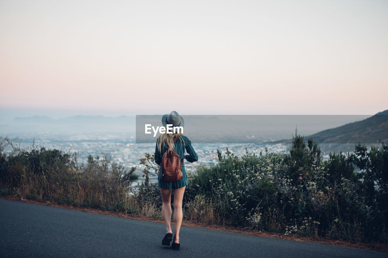 Rear view of woman walking on road against clear sky