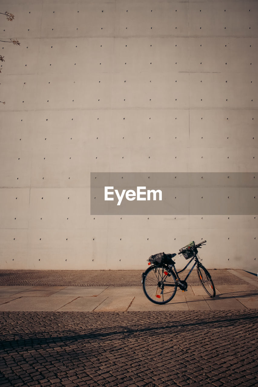 BICYCLE PARKED ON FOOTPATH AGAINST WALL IN CITY