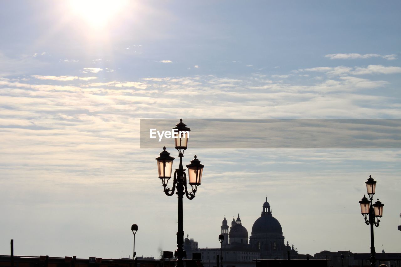 Street lights and silhouette church against sky during sunset