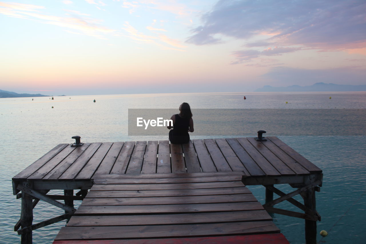 REAR VIEW OF WOMAN ON SEA AGAINST SKY