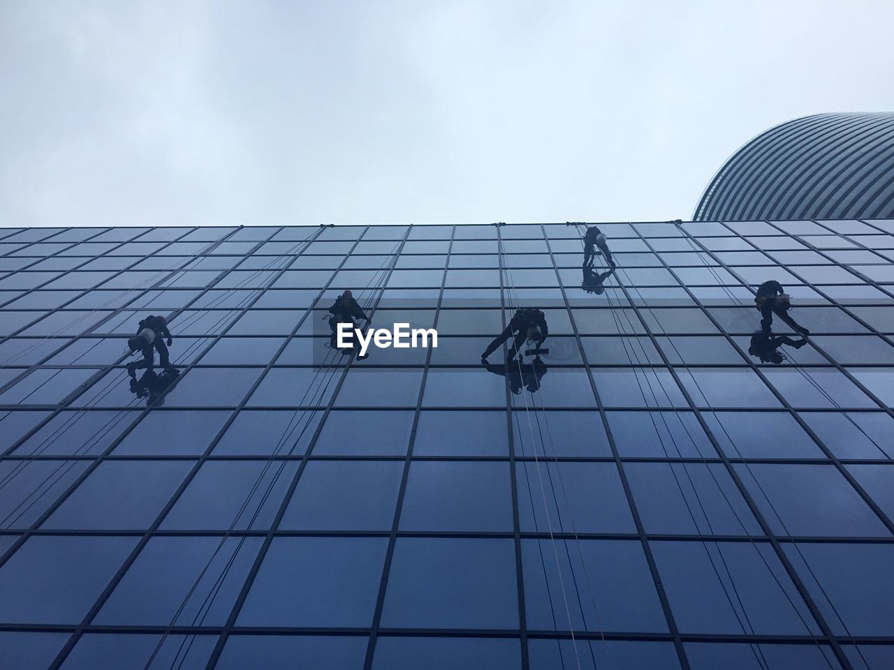 Low angle view of workers cleaning office building against sky