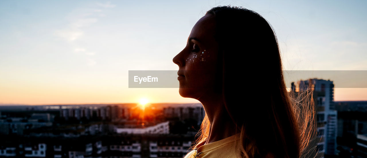 low angle view of young woman looking away against sky during sunset