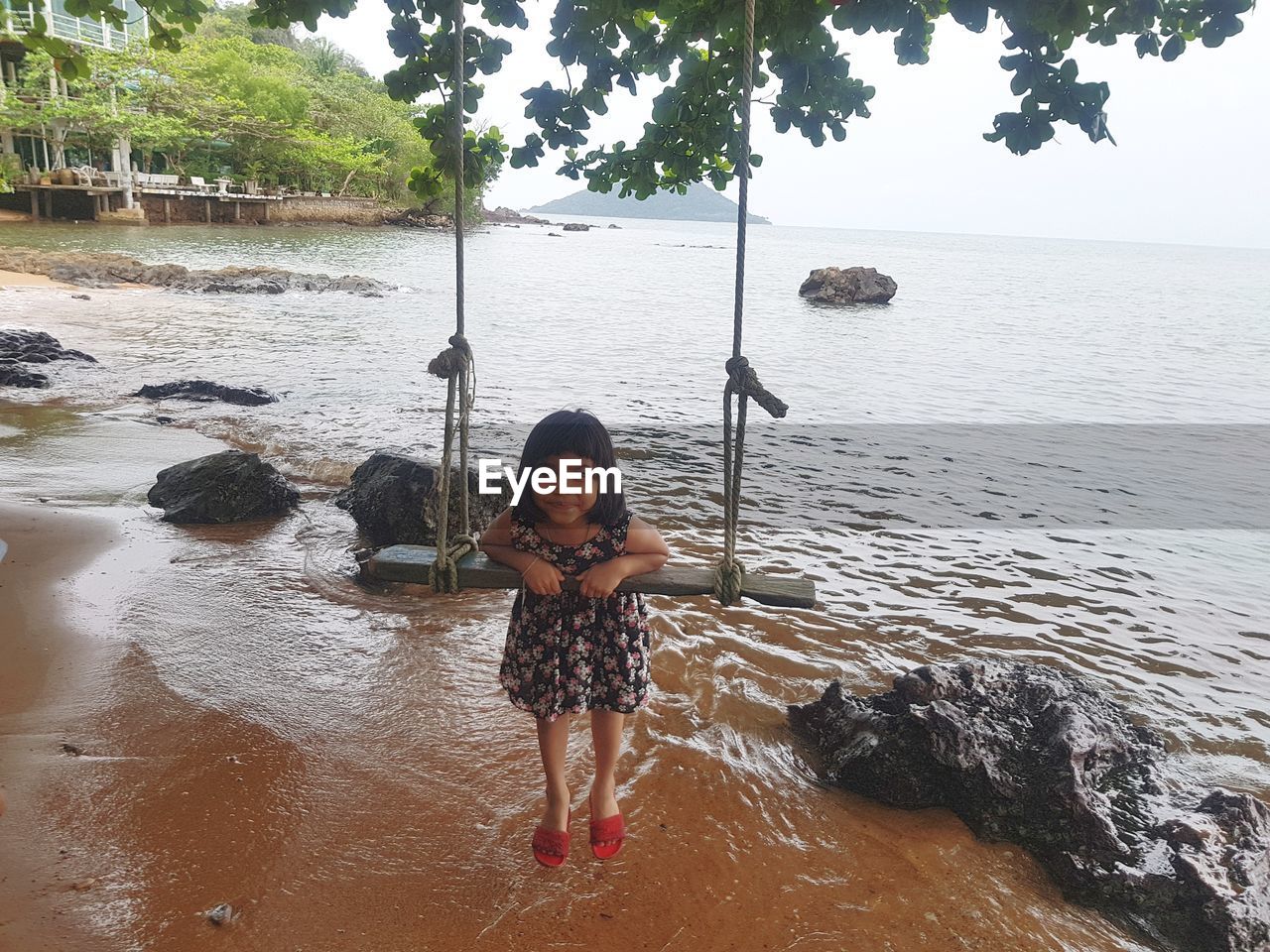 Portrait of smiling girl swinging at beach