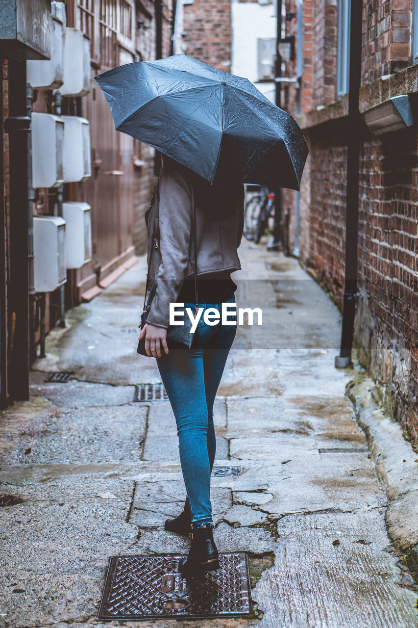 Full length of young woman holding umbrella while standing in alley