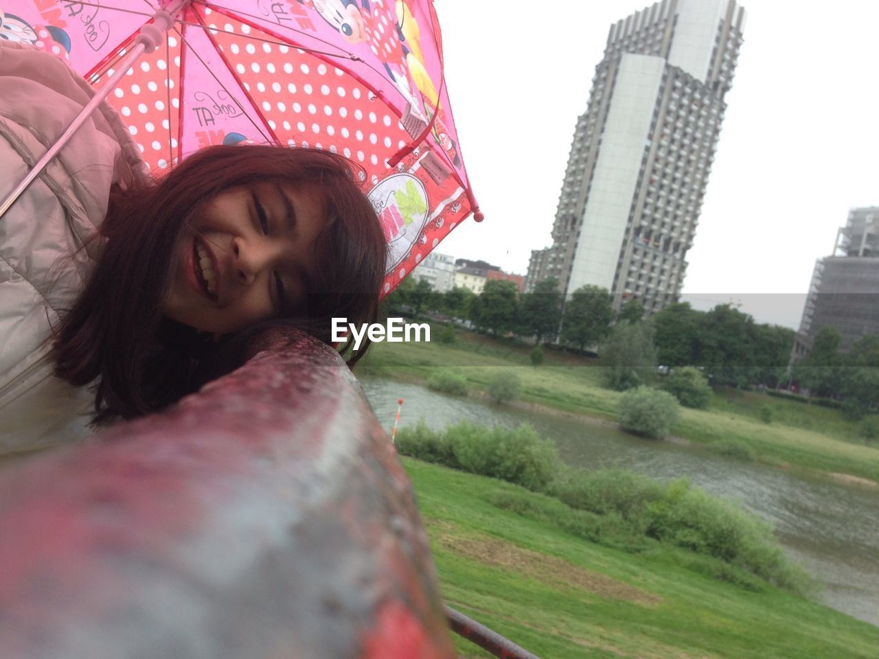 Portrait of smiling girl holding umbrella while leaning on railing during monsoon