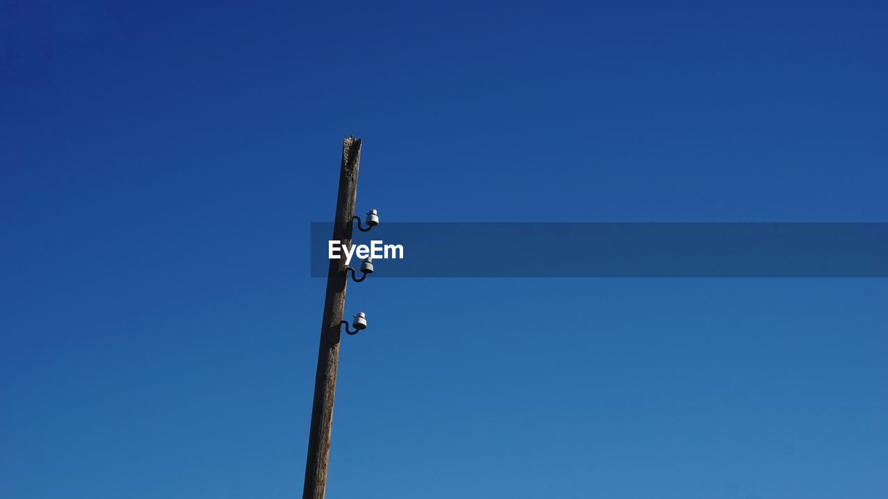 Low angle view of telephone pole against clear blue sky