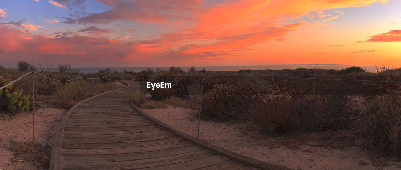 Scenic view of boardwalk against sky during sunset