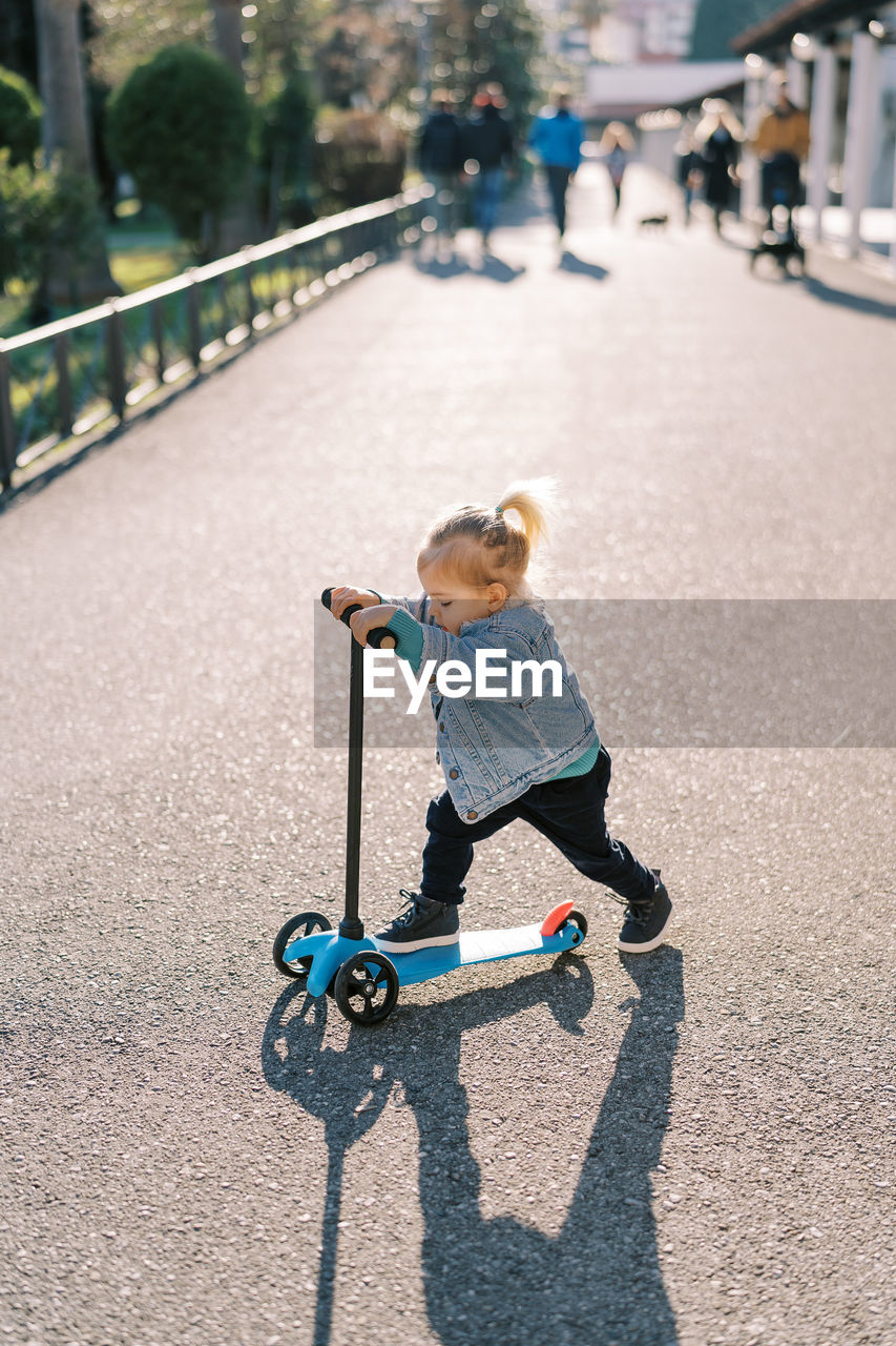 full length of boy riding push scooter on street