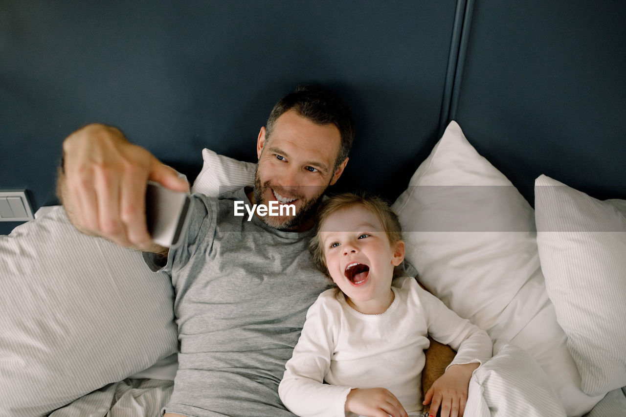 High angle view of father taking selfie with daughter on bed in hotel