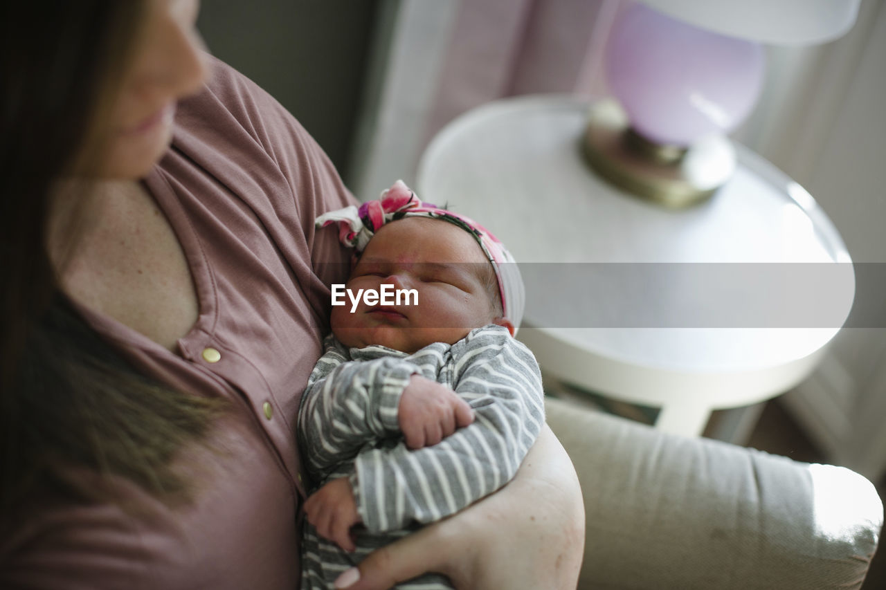 Midsection of mother carrying sleeping newborn daughter at home