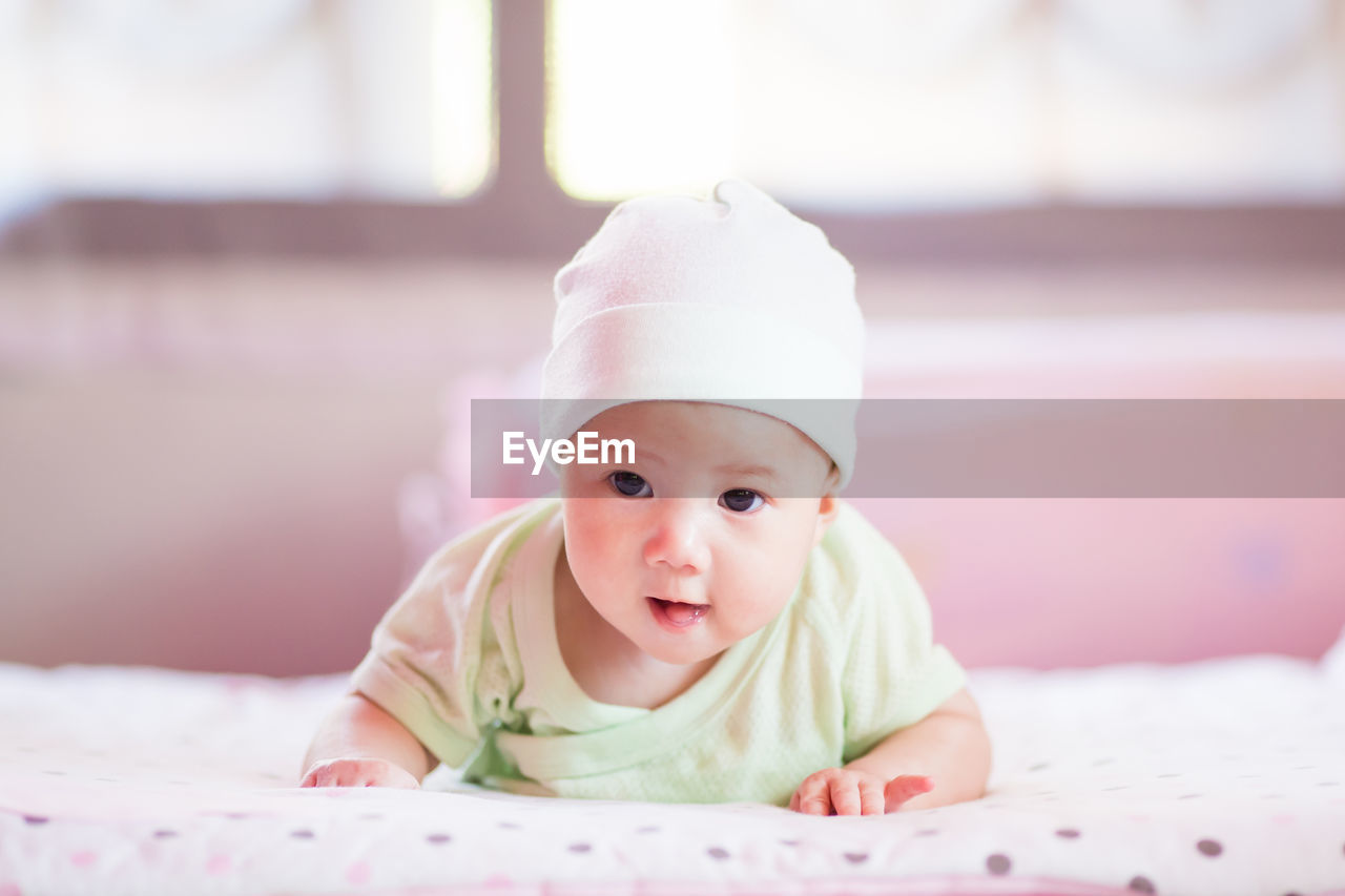 PORTRAIT OF CUTE BABY GIRL LYING ON BED AT HOME