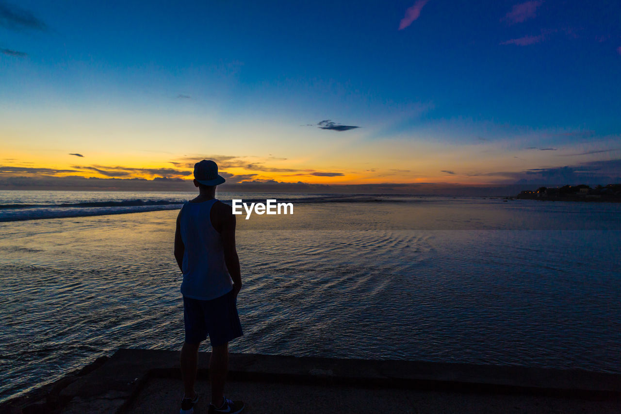 Rear view of man standing at beach during sunset