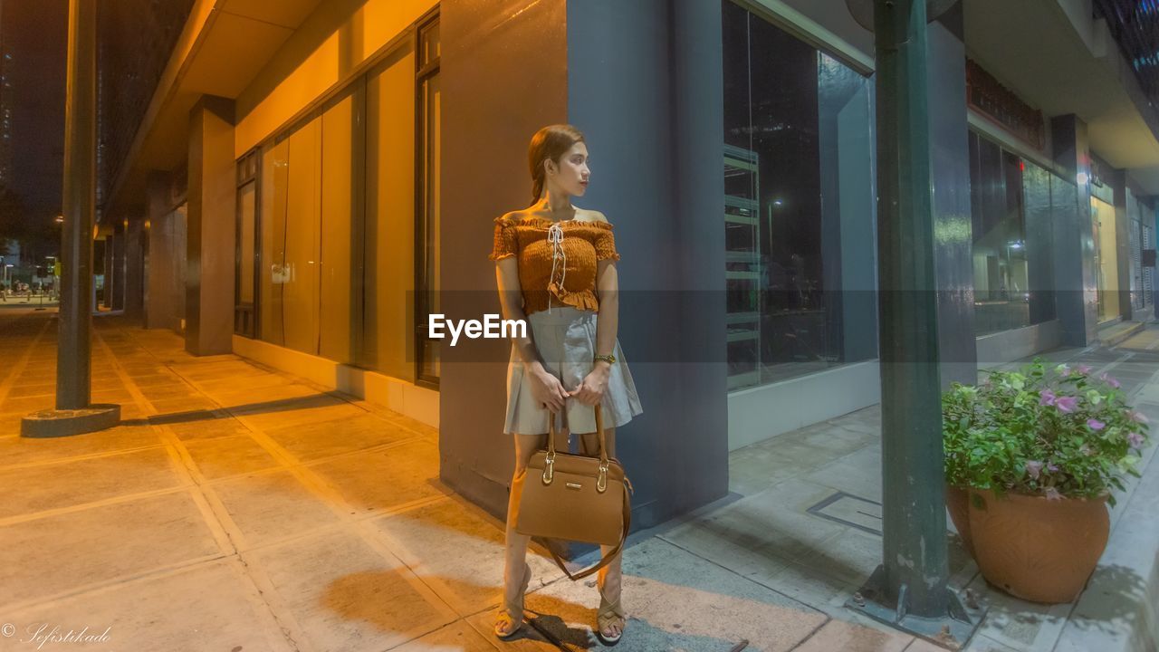 WOMAN STANDING BY GLASS BUILDING