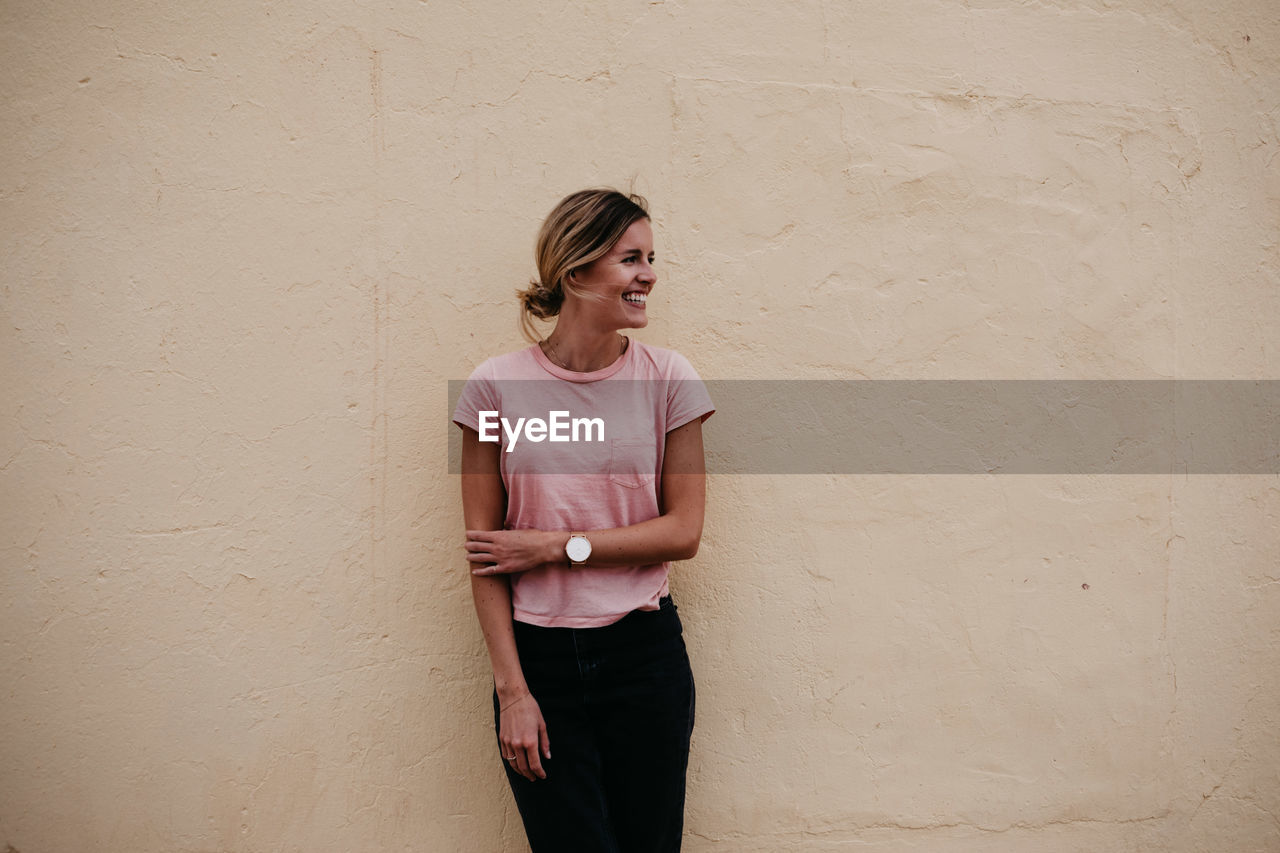 Woman looking away while standing against wall