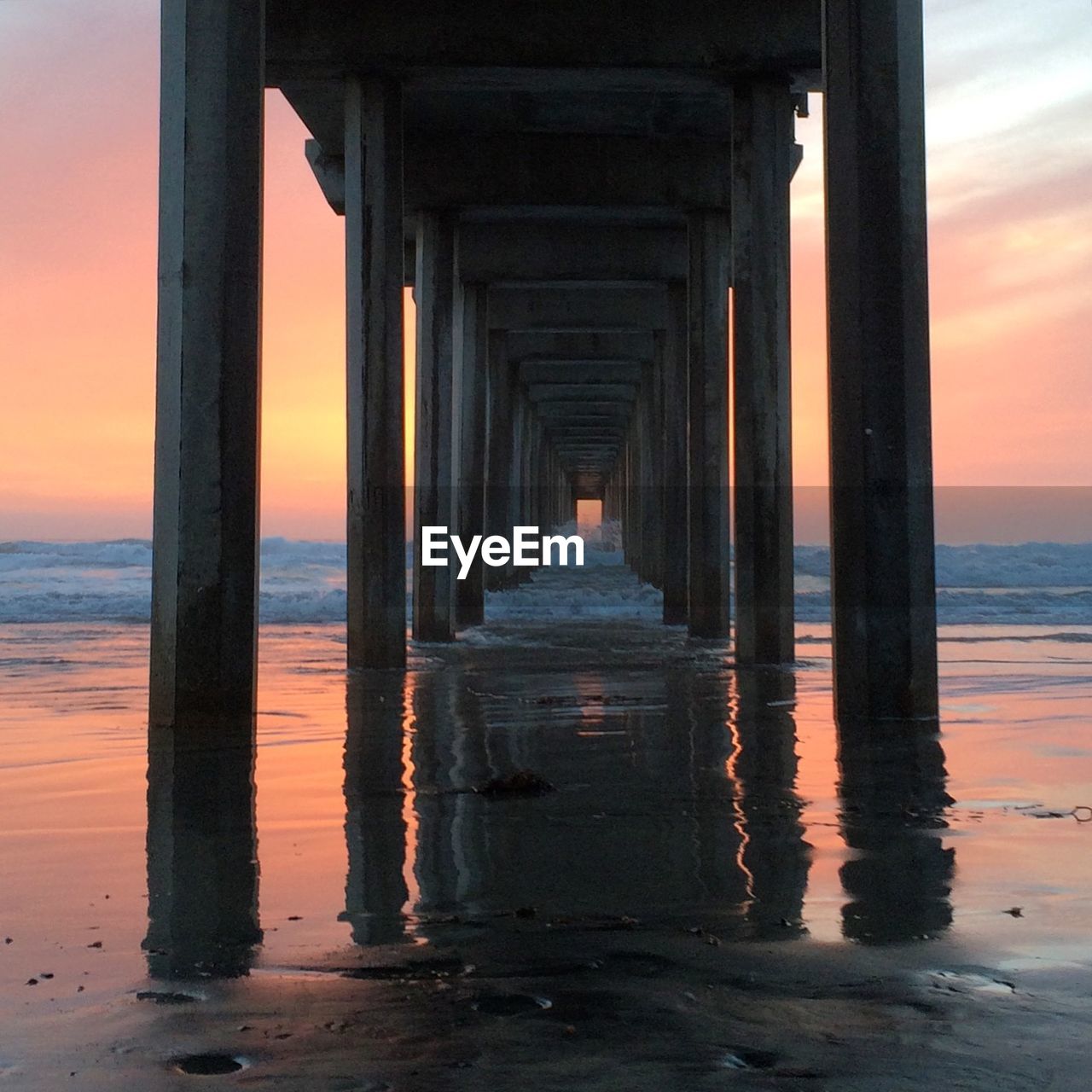 Waves rushing under pier against sky during sunset