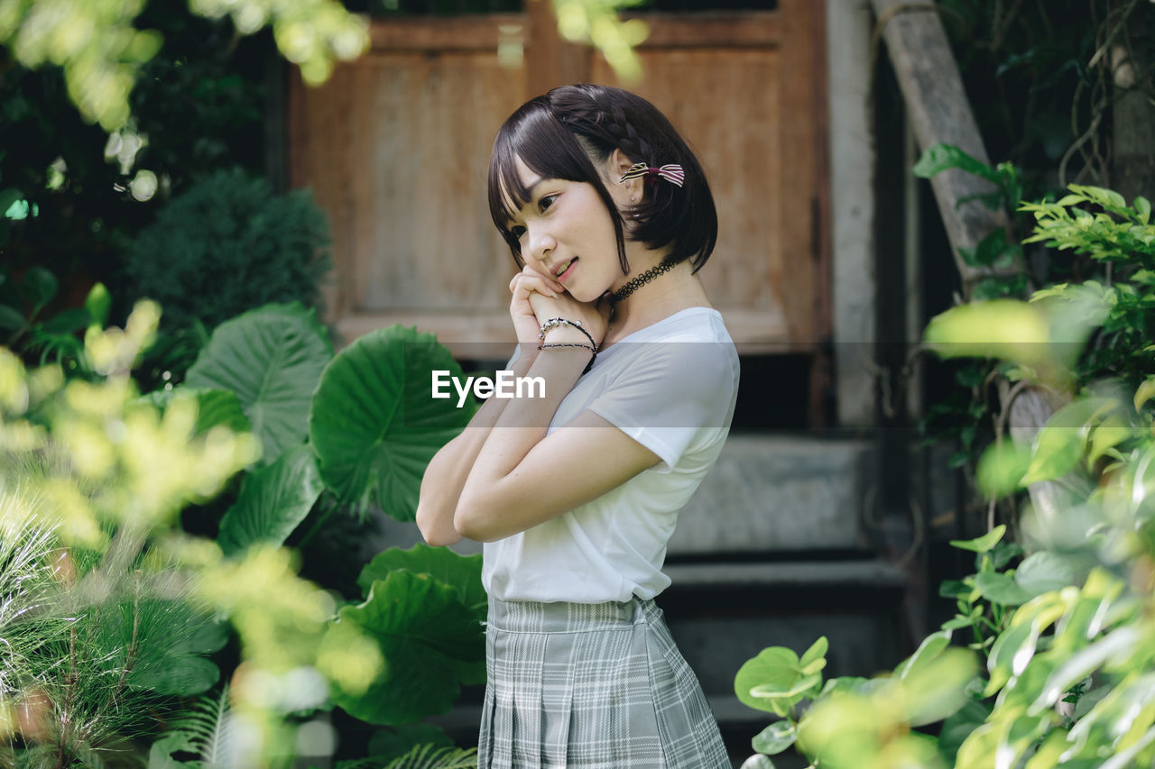 Side view of young woman standing against plants