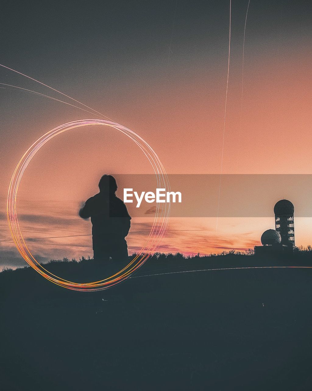 Silhouette boy spinning wire wool standing against sky during sunset