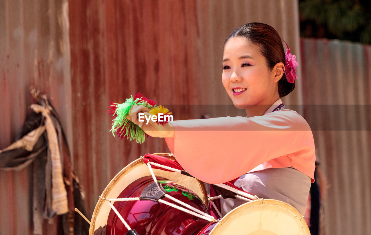 PORTRAIT OF SMILING YOUNG WOMAN STANDING AGAINST FLOWER