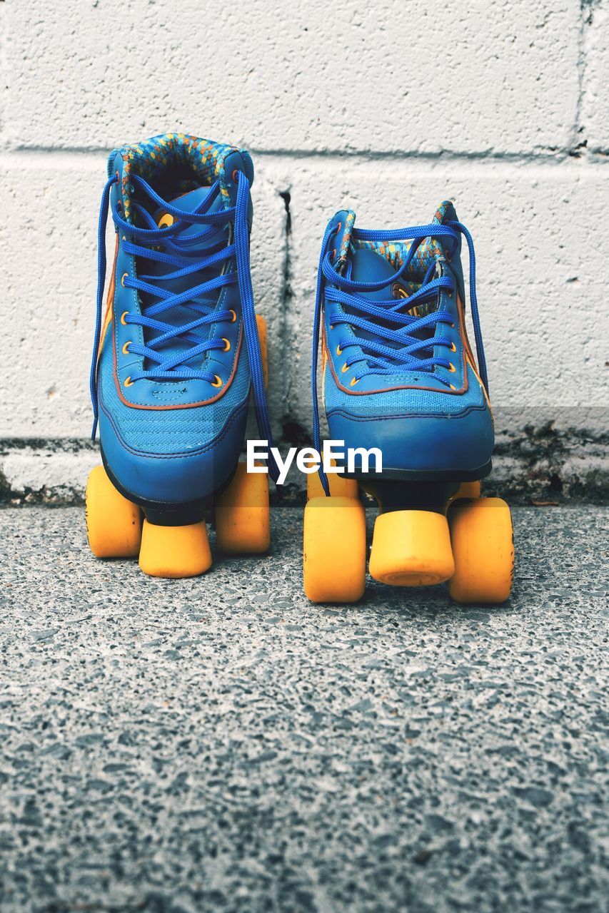 Closeup shot of blue vintage roller skates with orange wheels against white wall