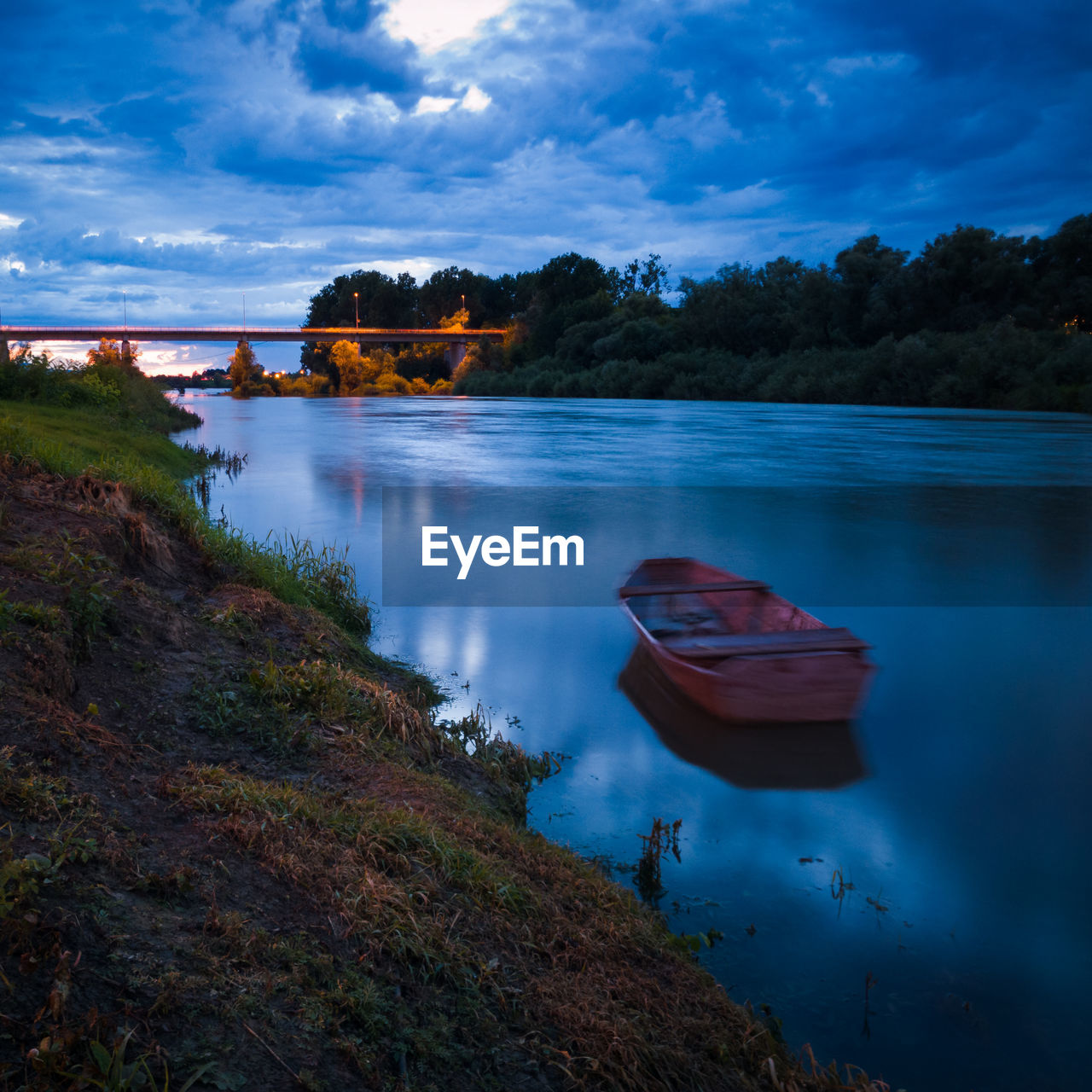 Landscape with moored boat in sava river during overcast evening at blue hour 