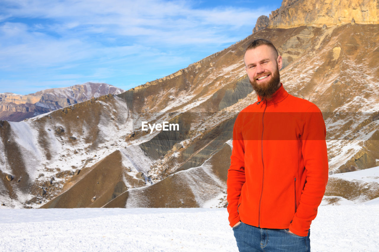 A cheerful bearded man with a brutal haircut in a red sweater on a sunny day against