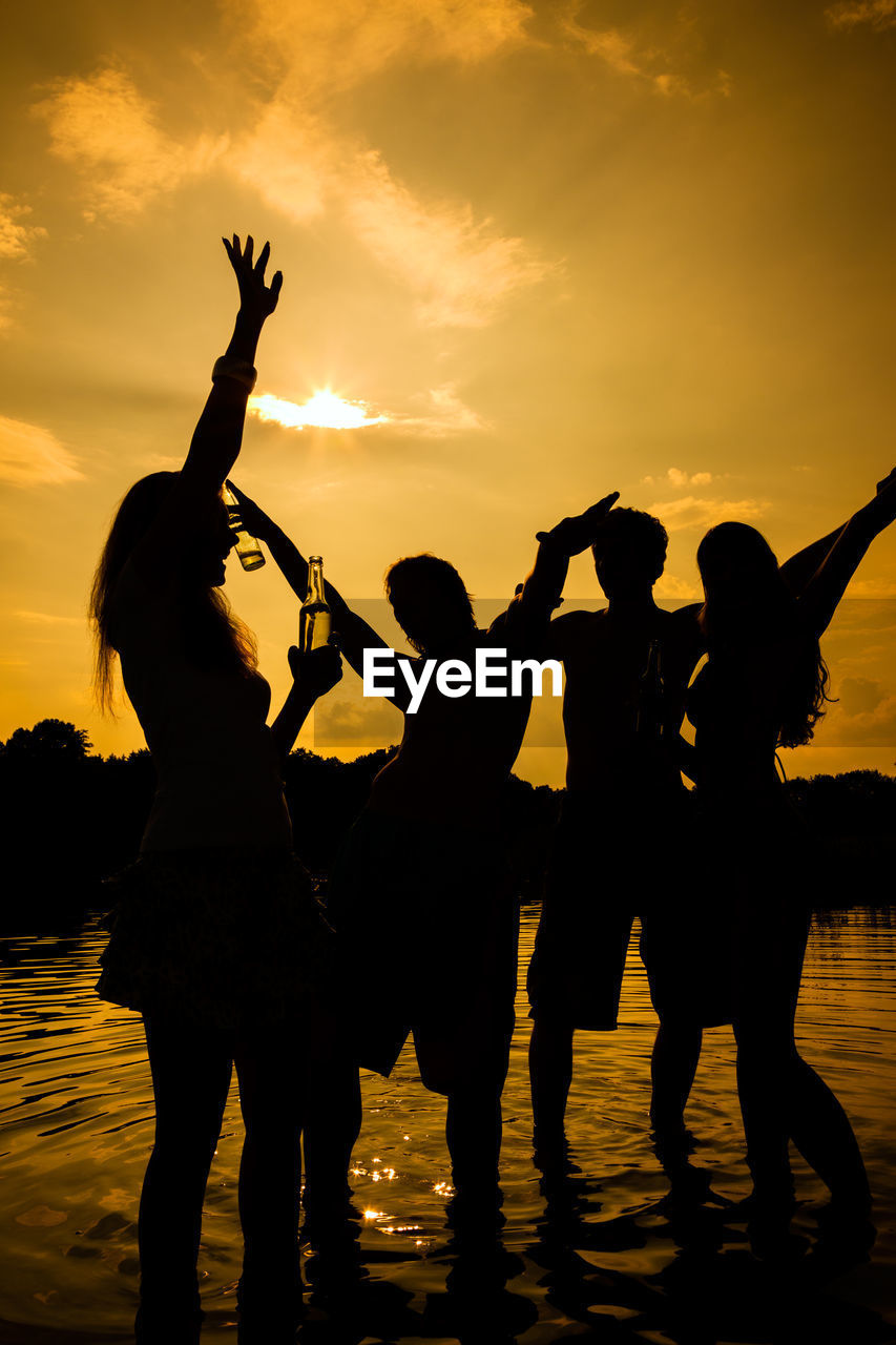 Silhouette people standing in lake against sky during sunset