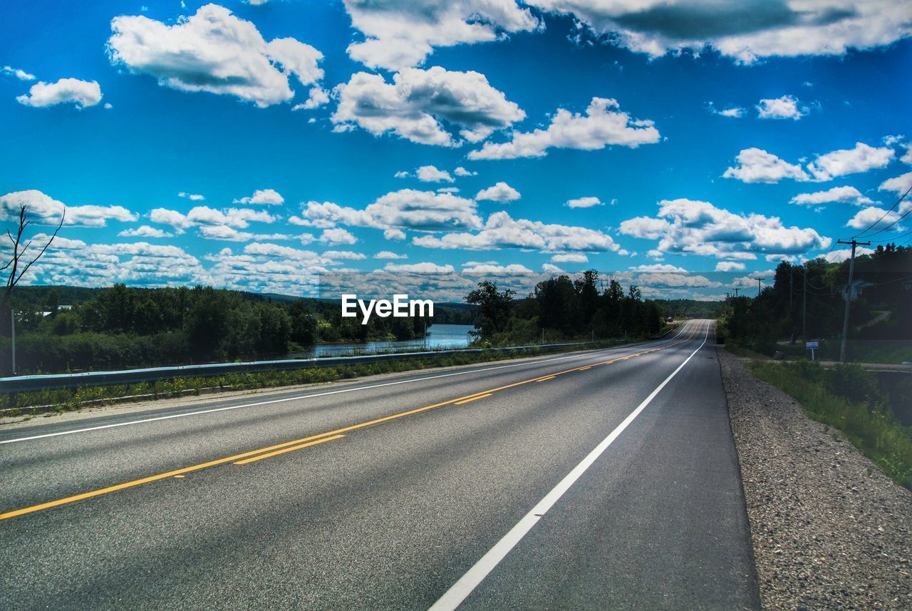 Empty road amidst field against cloudy sky