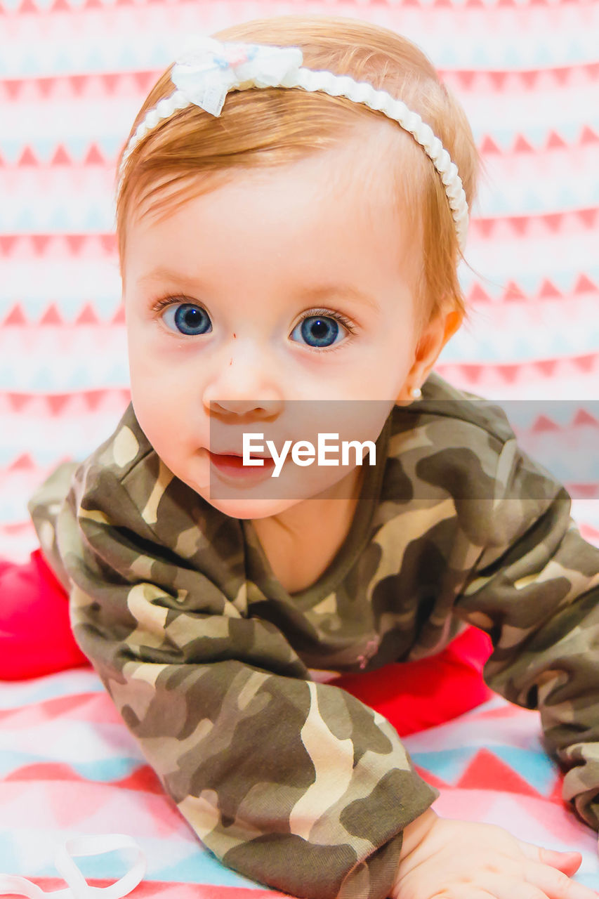 Portrait of cute baby girl sitting on bed