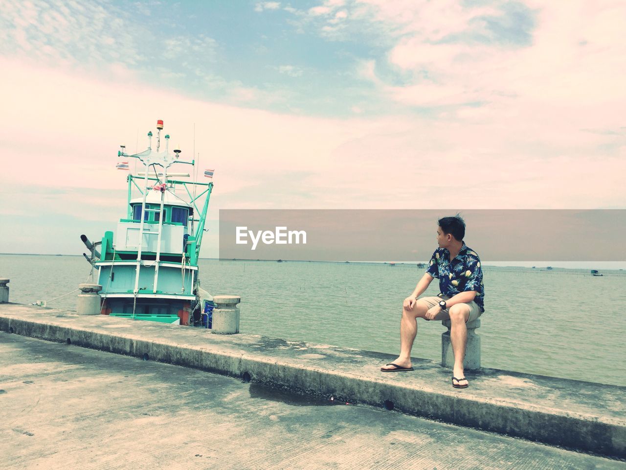 Man sitting on bollard against sea