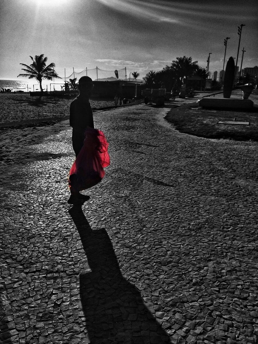 Side view of man standing on street while holding red bag