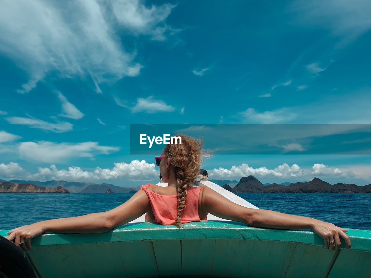 Rear view of woman sitting on boat in sea against blue sky