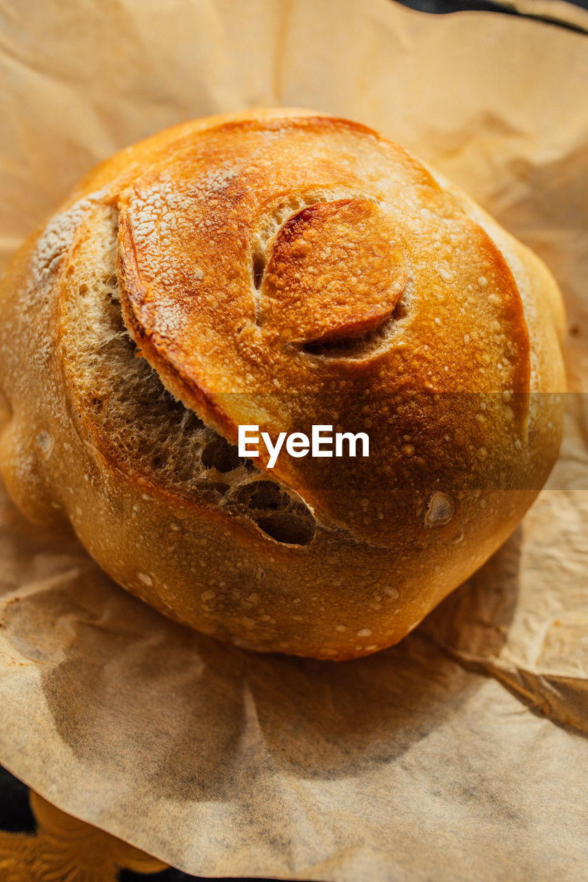 Freshly baked round loaf of homemade sourdough bread on brown parchment paper