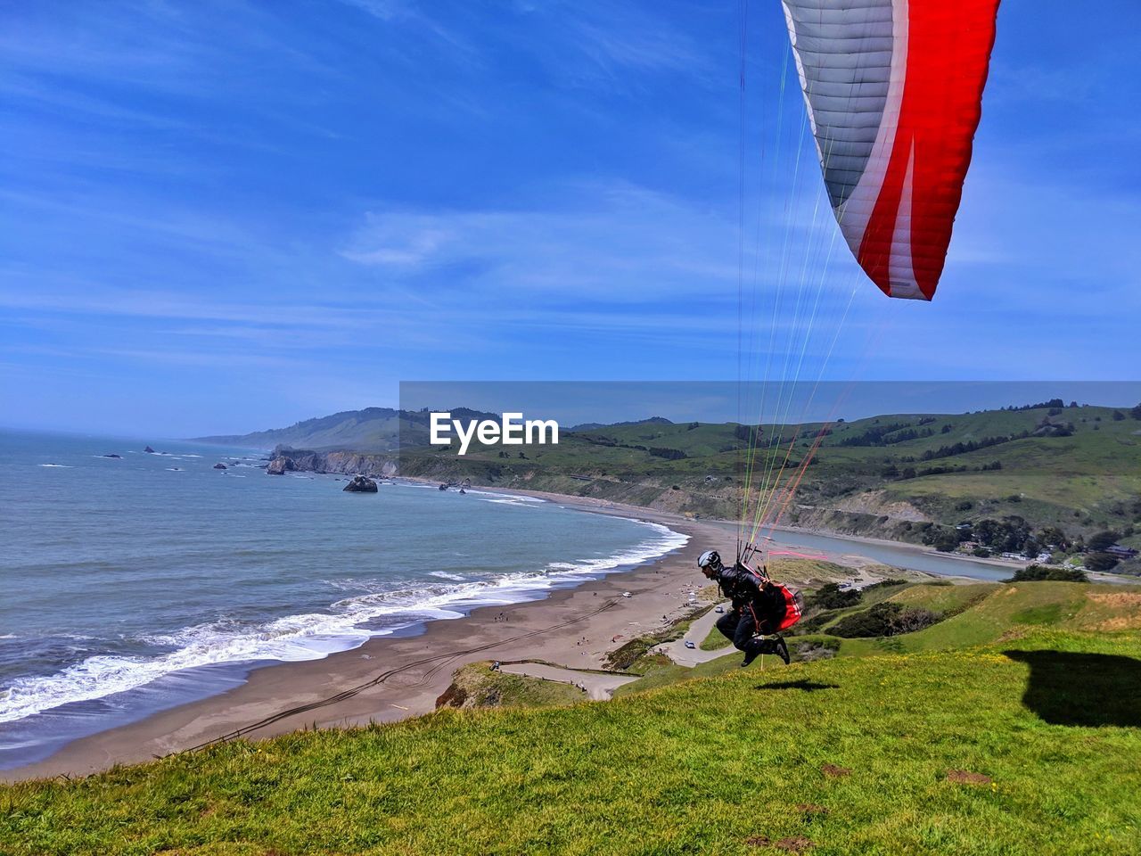 Paraglider jumping off cliff against blue ocean background.