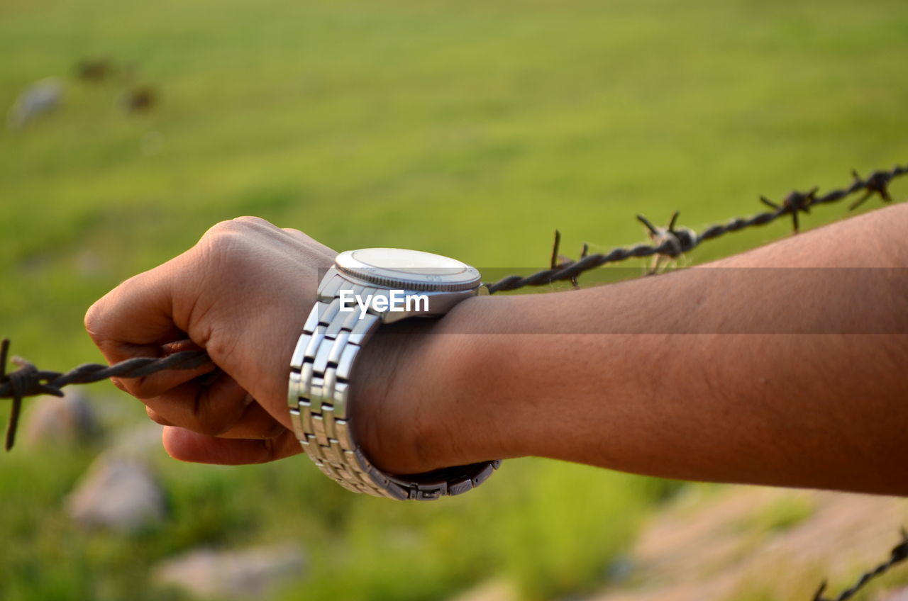 Cropped image of hand wearing wristwatch holding barbed wire