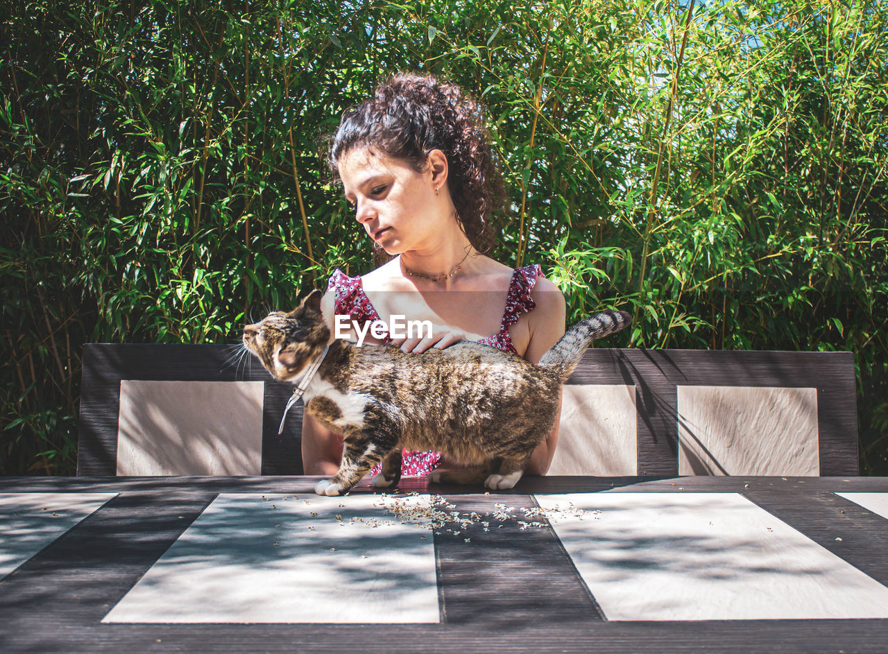 Young girl with her cat sitting at the table against bamboo leaves