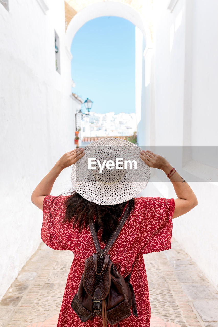 Back view of unrecognizable female tourist with raised arms on narrow street between old houses in greece