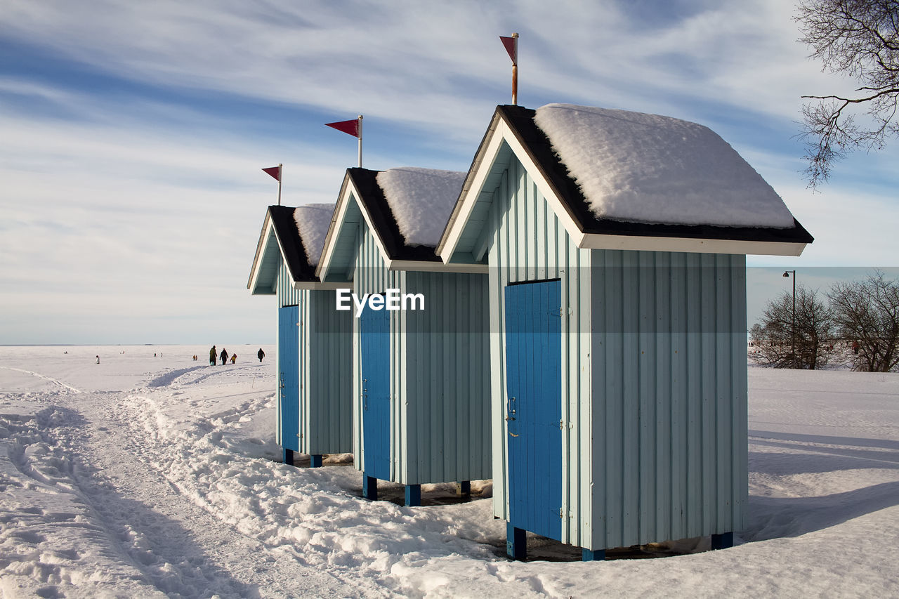Three old beach huts stand empty on a beautiful winter day. people are walking on the ice.