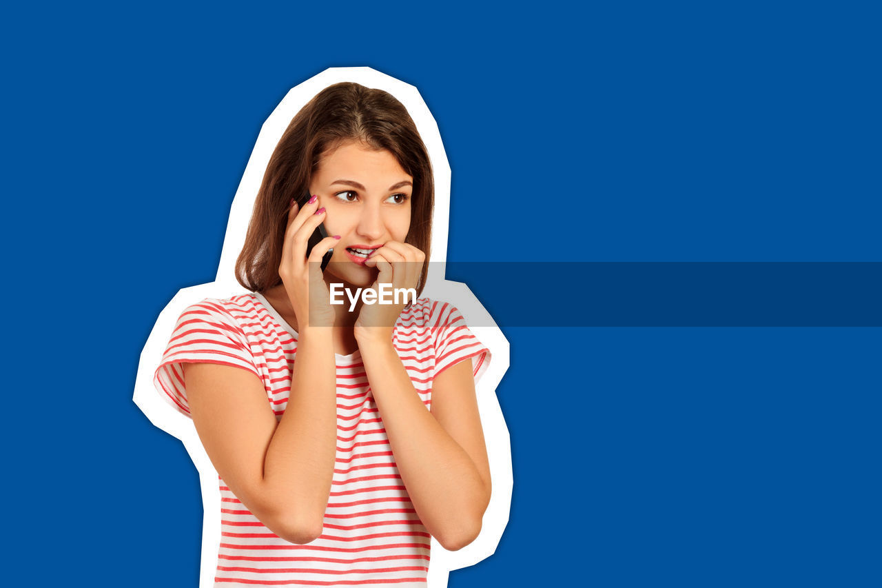 Shocked young woman talking over mobile phone cut out against blue background