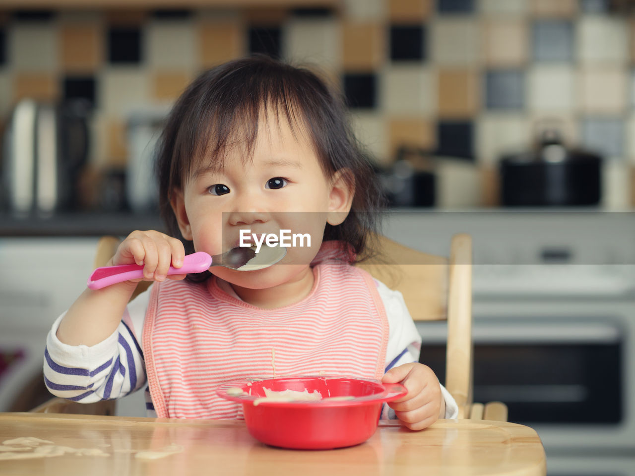 Portrait of baby girl eating food while sitting on high chair at home